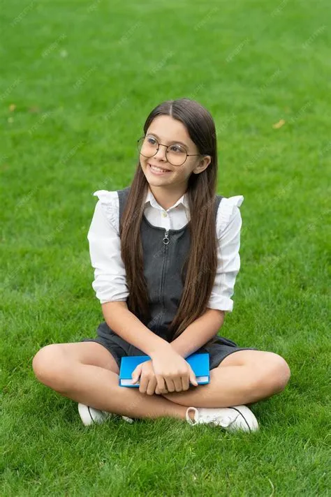 Premium Photo | Happy teen school girl sitting legs crossed on grass ...
